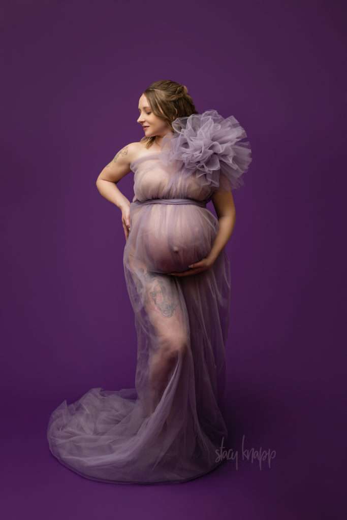 Maternity photo of a pregnant Maine mother in a purple gown with a dark purple background by photographer Stacy Knapp Photography