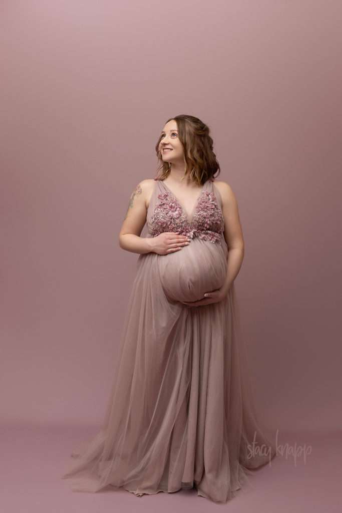 Maternity photo of a pregnant Maine mother in a pink floral gown with a pink background by photographer Stacy Knapp Photography