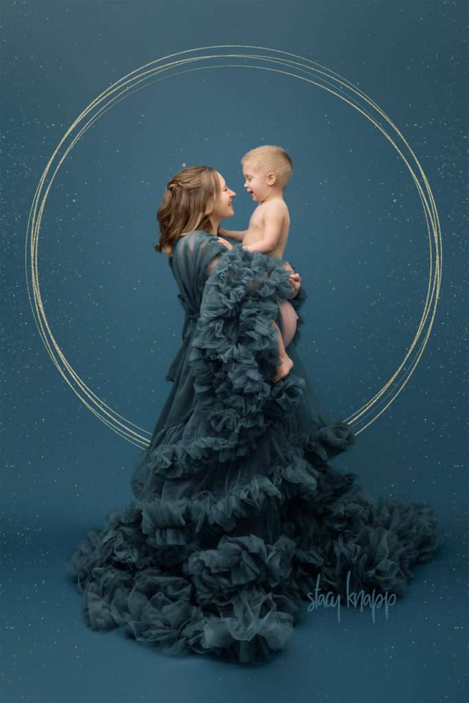 Photo of a young Maine mother wearing a teal luxury maternity gown holding her toddler baby boy while pregnant with a baby girl by photographer Stacy Knapp Photography