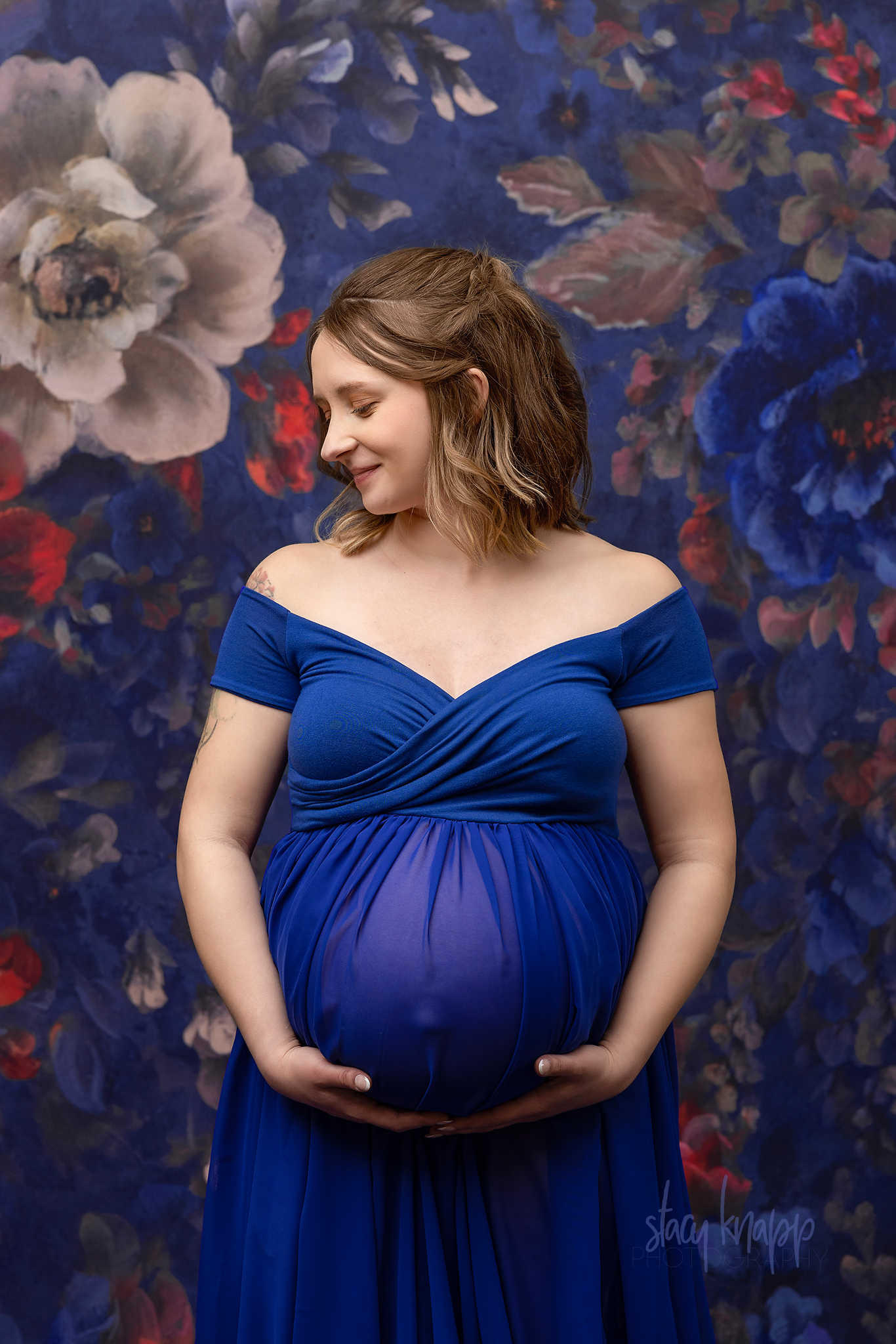 Close-up maternity photo of a pregnant Maine mother in a blue gown with a floral background by photographer Stacy Knapp Photography