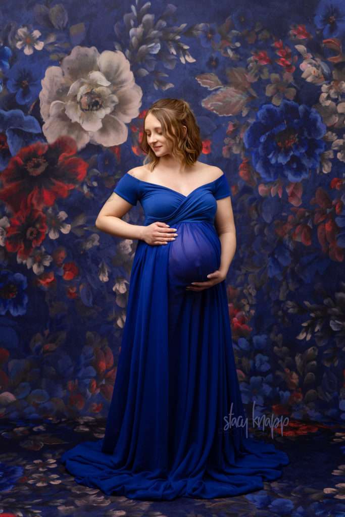 Maternity photo of a pregnant Maine mother in a blue gown with a floral background by photographer Stacy Knapp Photography