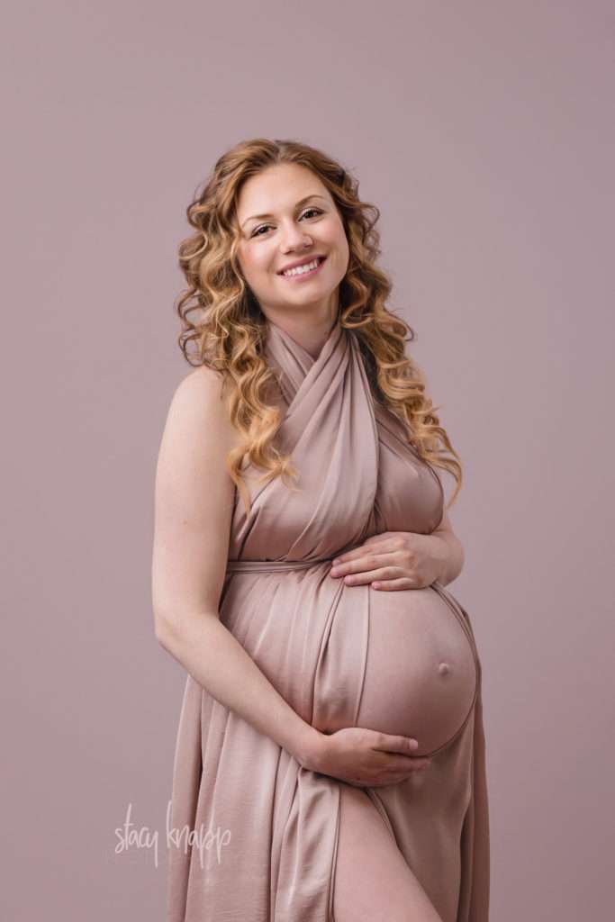 Maternity photo of a pregnant Maine mother wrapped in pink fabric with a pink background by photographer Stacy Knapp Photography