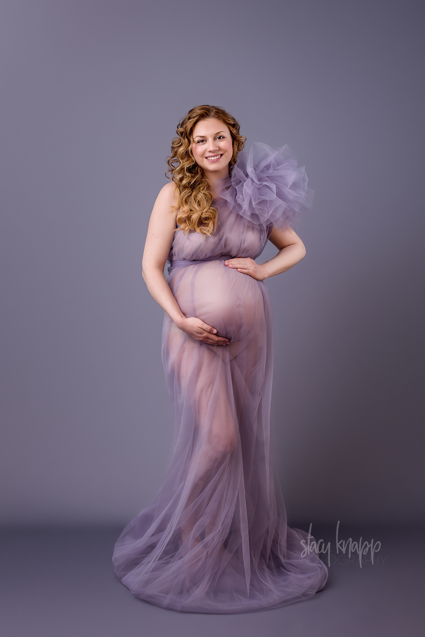Maternity photo of a pregnant Maine mother in a purple gown with a grey background by photographer Stacy Knapp Photography
