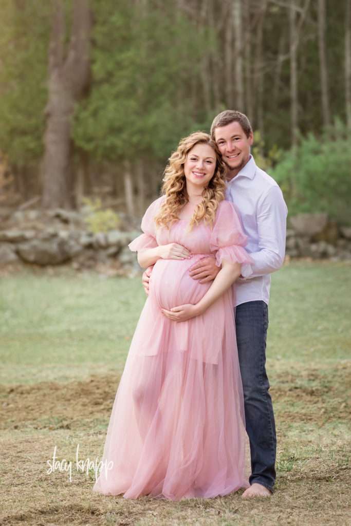 Maternity photo of a pregnant Maine mother in a pink gown with her husband outside by photographer Stacy Knapp Photography