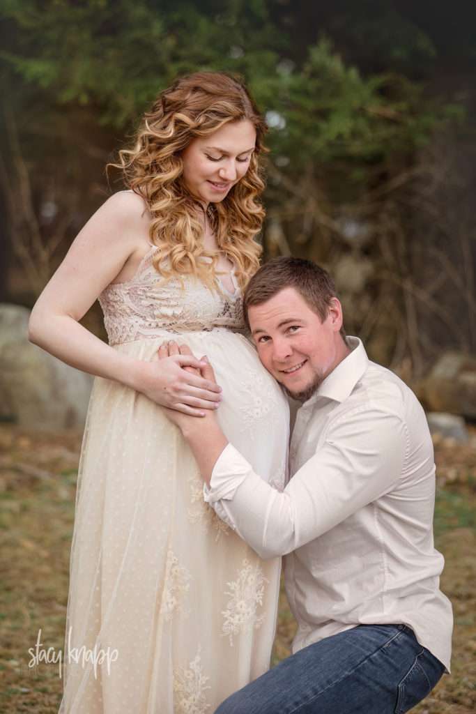 Maternity photo of a pregnant Maine mother in a cream gown with her husband outdoors on location by photographer Stacy Knapp Photography