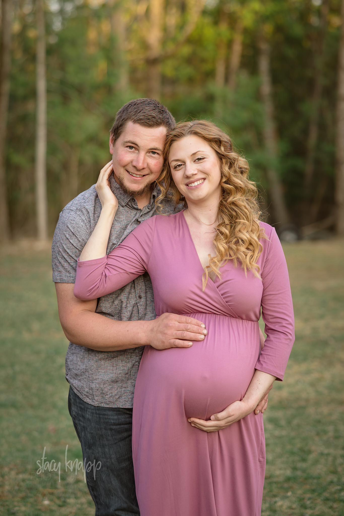 Maternity photo of a pregnant Maine mother in a pink dress with her husband outside on location by photographer Stacy Knapp Photography