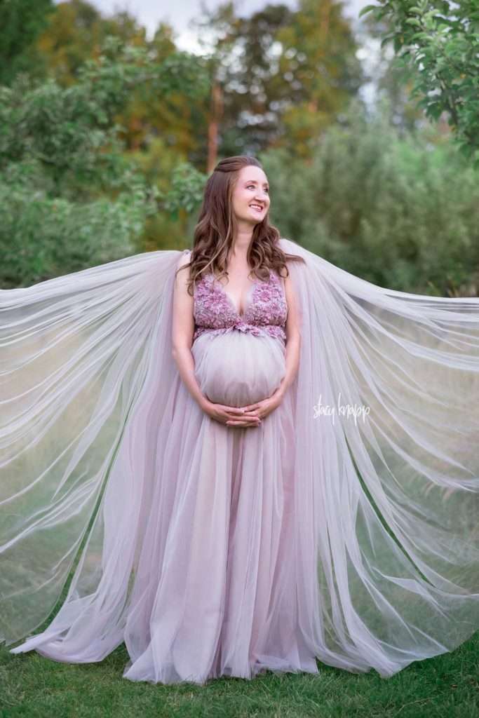Maine maternity photo of a pregnant mother in pink gown standing in front of apple trees in the Viles Arboretum in Augusta by photographer Stacy Knapp Photography