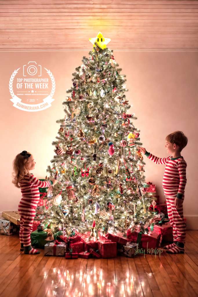 Christmas photo of two Maine children standing near tree covered in lights and holiday decorations