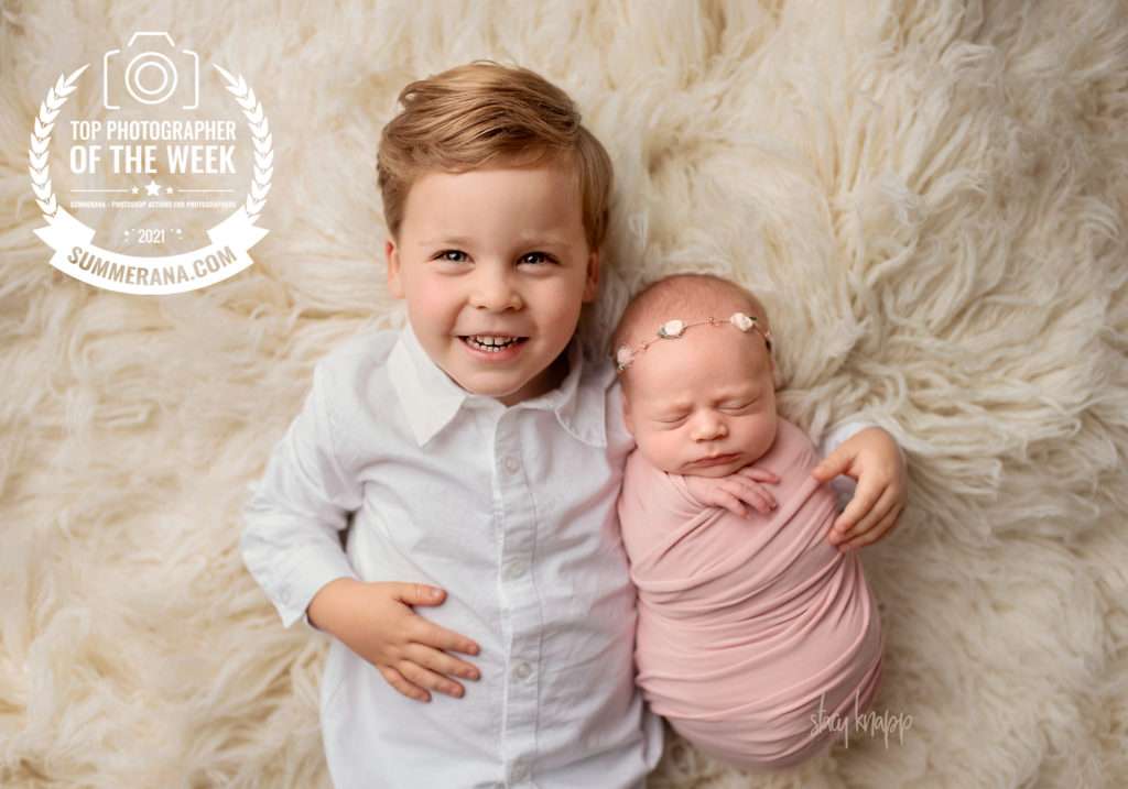 Photo of Maine newborn wearing pink wrap and snuggling with baby bother